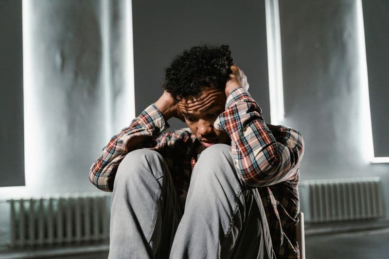 A man sits with his head in his hands, visibly distressed