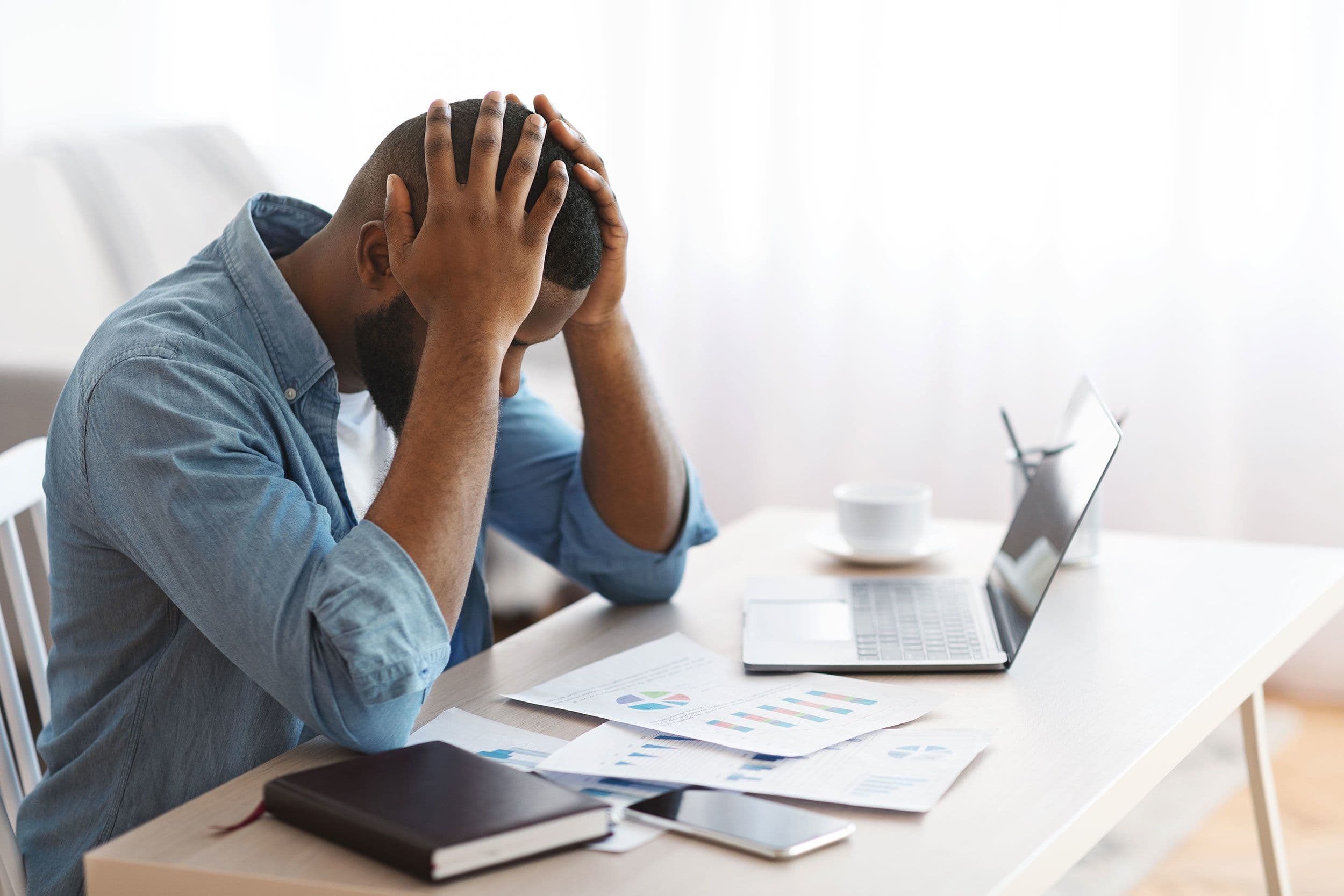 A man rests his head in his hand at a desk covered in work