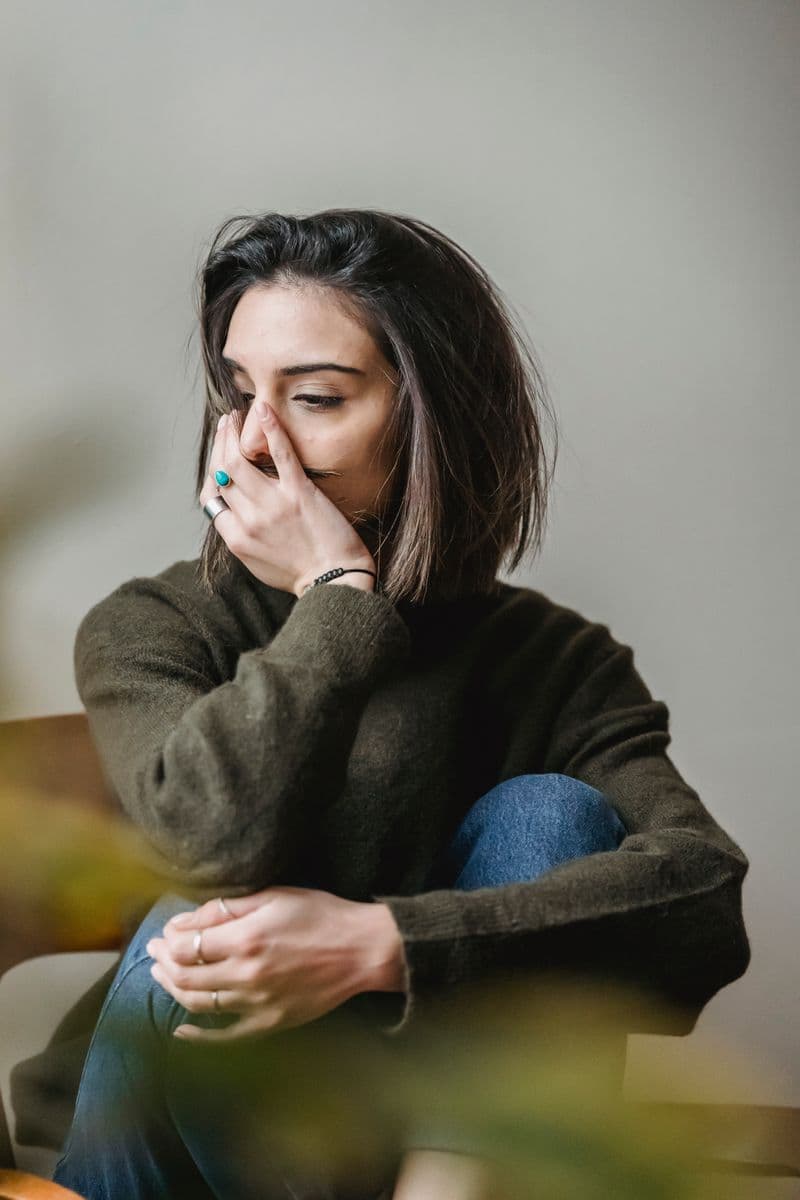 A woman sits quietly with her hand to her face, lost in thought