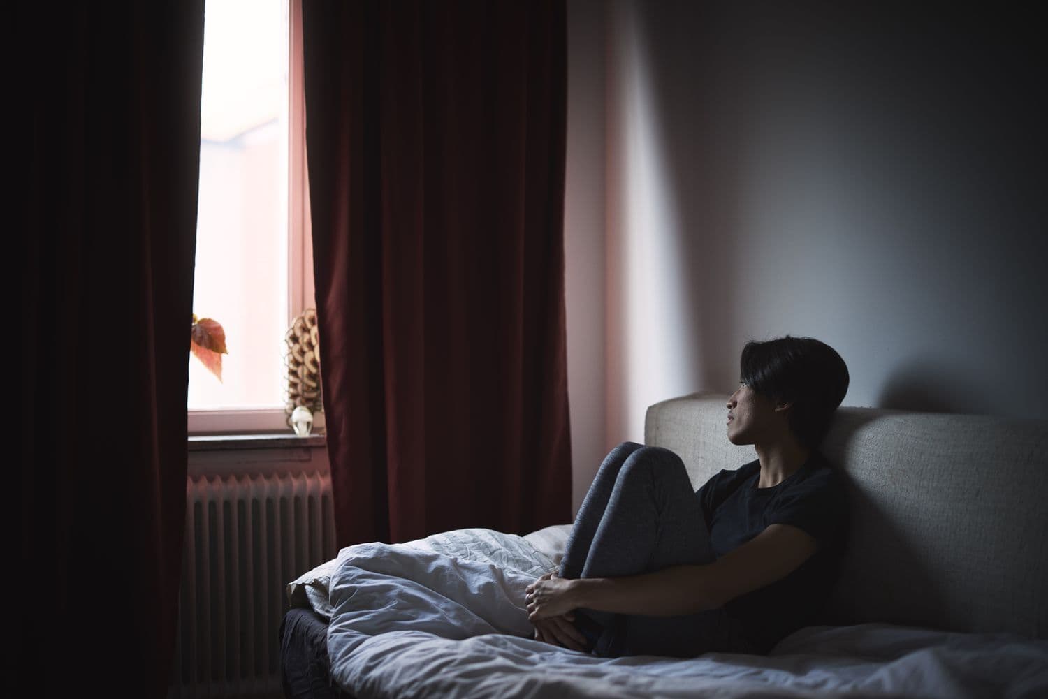 A silhouetted figure stands alone at a lit window in a dark room