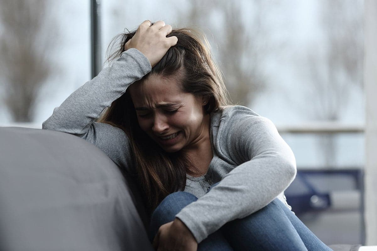 A woman sits crying with her hand in her hair, visibly distressed